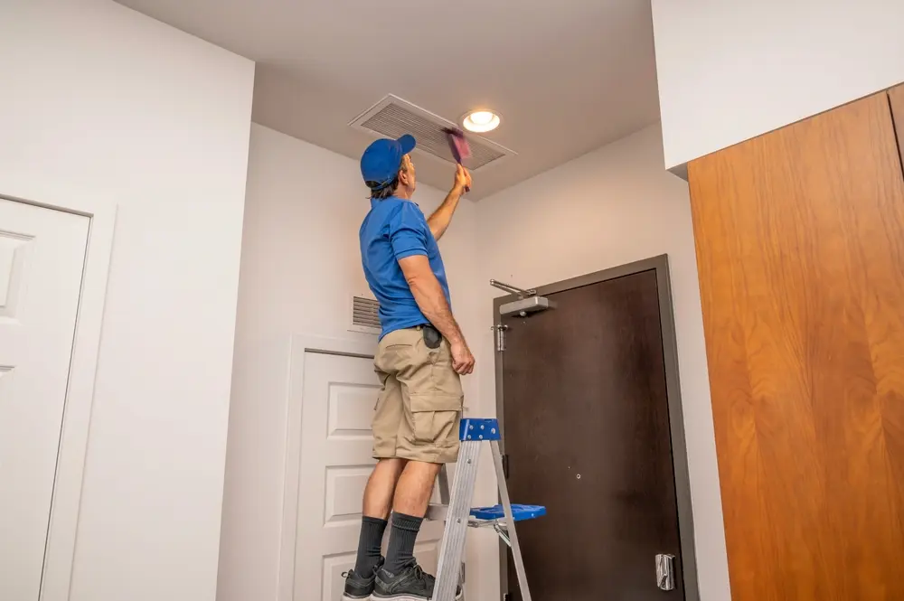Handyman on a ladder cleaning a return air duct inside of a home